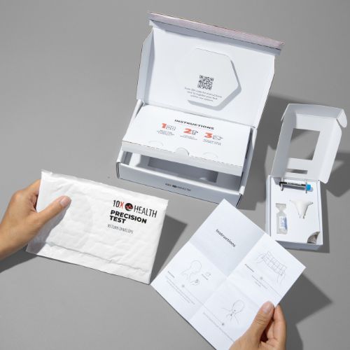 hands holding a packet and instructions for the 10X Health Precision Test with the box and other materials sitting on a grey counter nearby