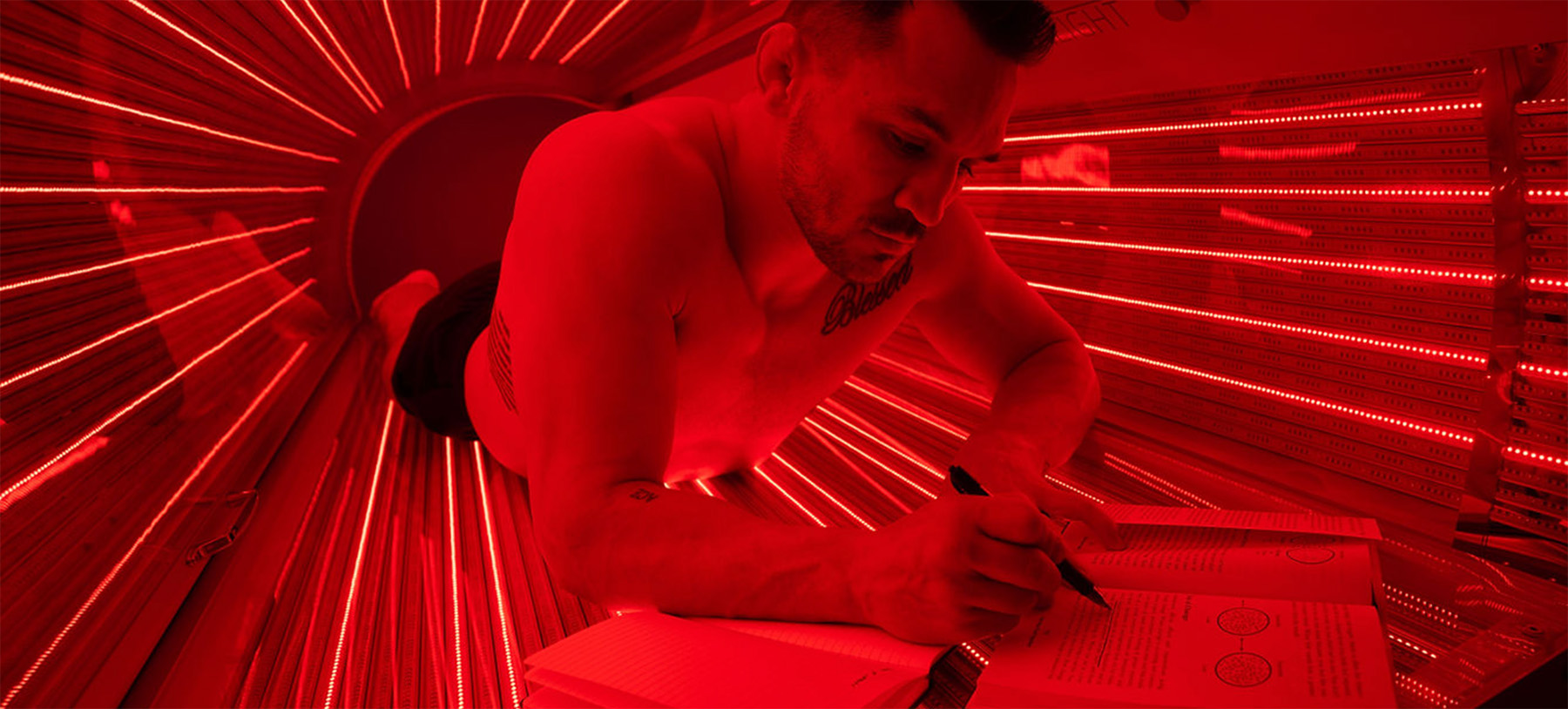 a man taking notes while reading a book inside a red light therapy bed